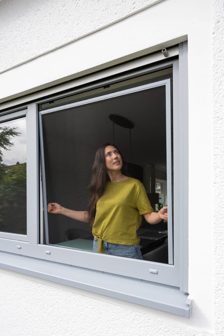 Maßgefertigter Fliegengitter-Spannrahmen in Ubstadt-Weiher an einem Fenster mit Frau im Innenraum
