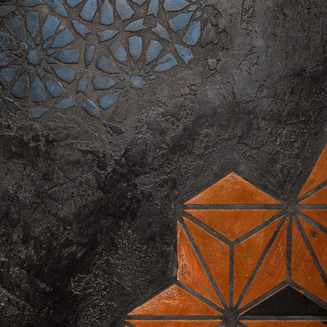 Dunkle Oberfläche mit blauer Ornamentik und kupferfarbenen Geometrie-Elementen